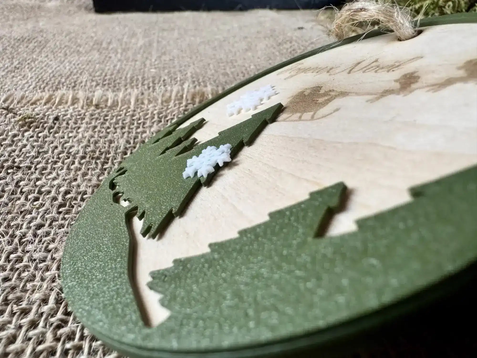 Boule de noel en bois gravée avec le texte Joyeux Noël, des sapins en premier plan et des flocons imprimés en PLA Biodégradable, vu zoomée