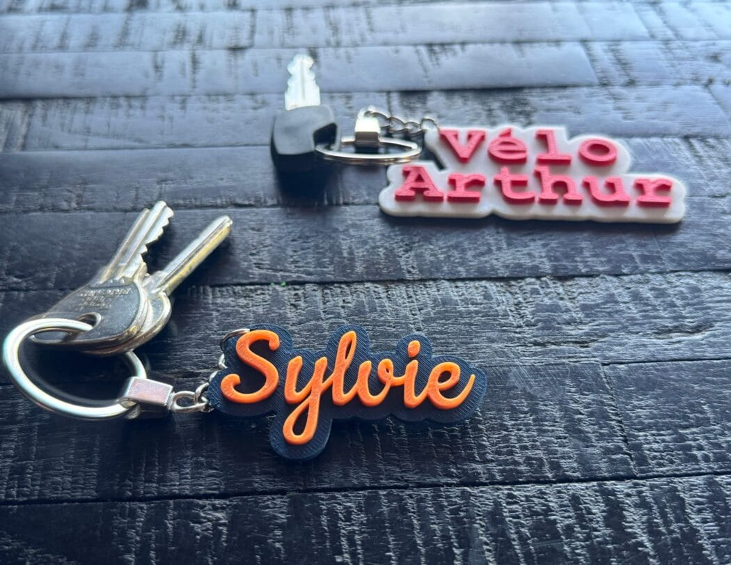 Personalized key ring made in France - Two sets of keys, in the foreground one with a Sylvie key ring in intense blue and orange lettering, in the background, a white Vélo Arthur key ring and red lettering