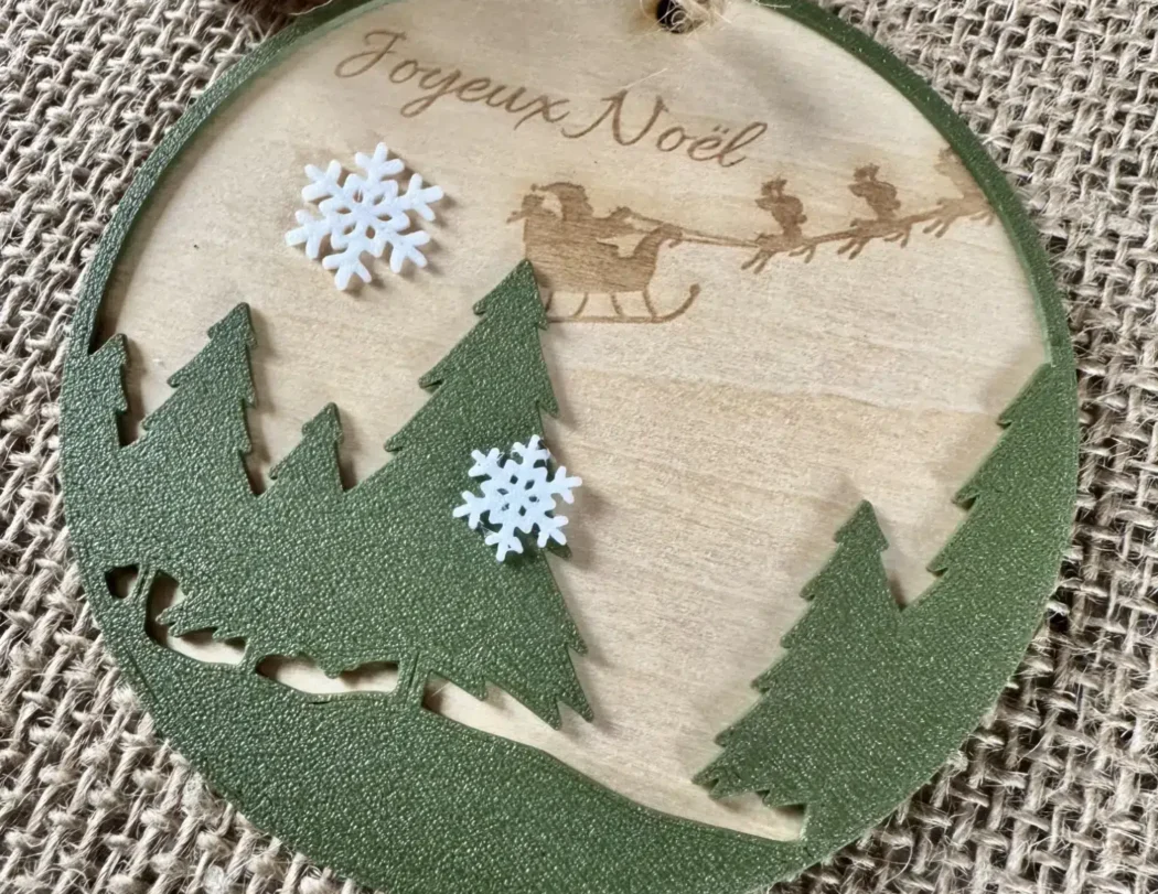 Wooden Christmas ball engraved with the text Merry Christmas, fir trees in the foreground and snowflakes printed in Biodegradable PLA