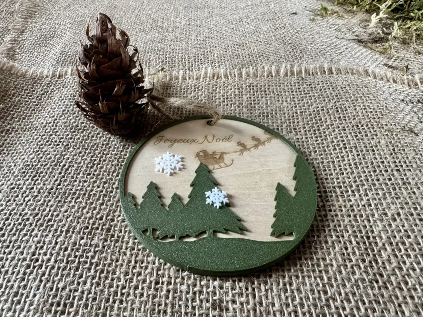 Wooden Christmas ball engraved with the text Merry Christmas, fir trees in the foreground and snowflakes printed in Biodegradable PLA