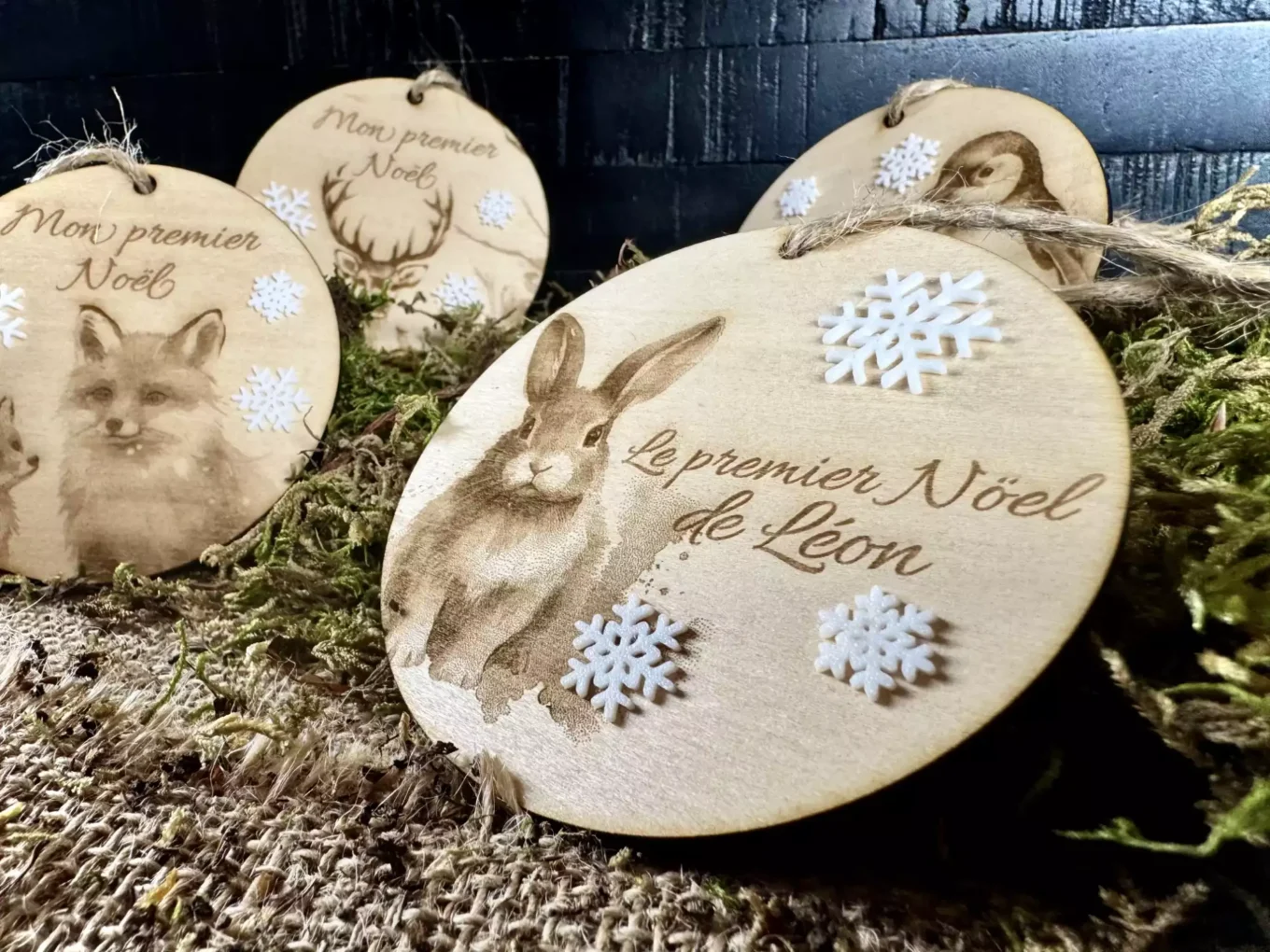 Une boule de Noël personnalisée en bois, elle représente un lièvre avec le texte Le premier Noël de Léon. Des petits flocons blanc en PLA biodégrable sont collés dessus